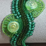 photo of Green River Bracelet using different sized green seed beads in a wavy herringbone stitch and two round disc beads with waves of green bugle beads on either side of the bracelet by Amanda Crago of Bowerbird Jewellery