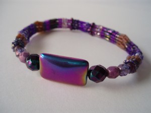 photo of a purple bangle using seed beads, bugle beads and a large rectangular purple oil slick coloured bead as the focal