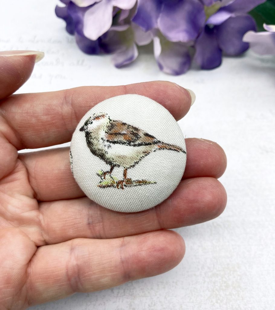 colour photo of a handmade fabric button brooch featuring a coloured sketch of a house sparrow by Bowerbird Jewellery